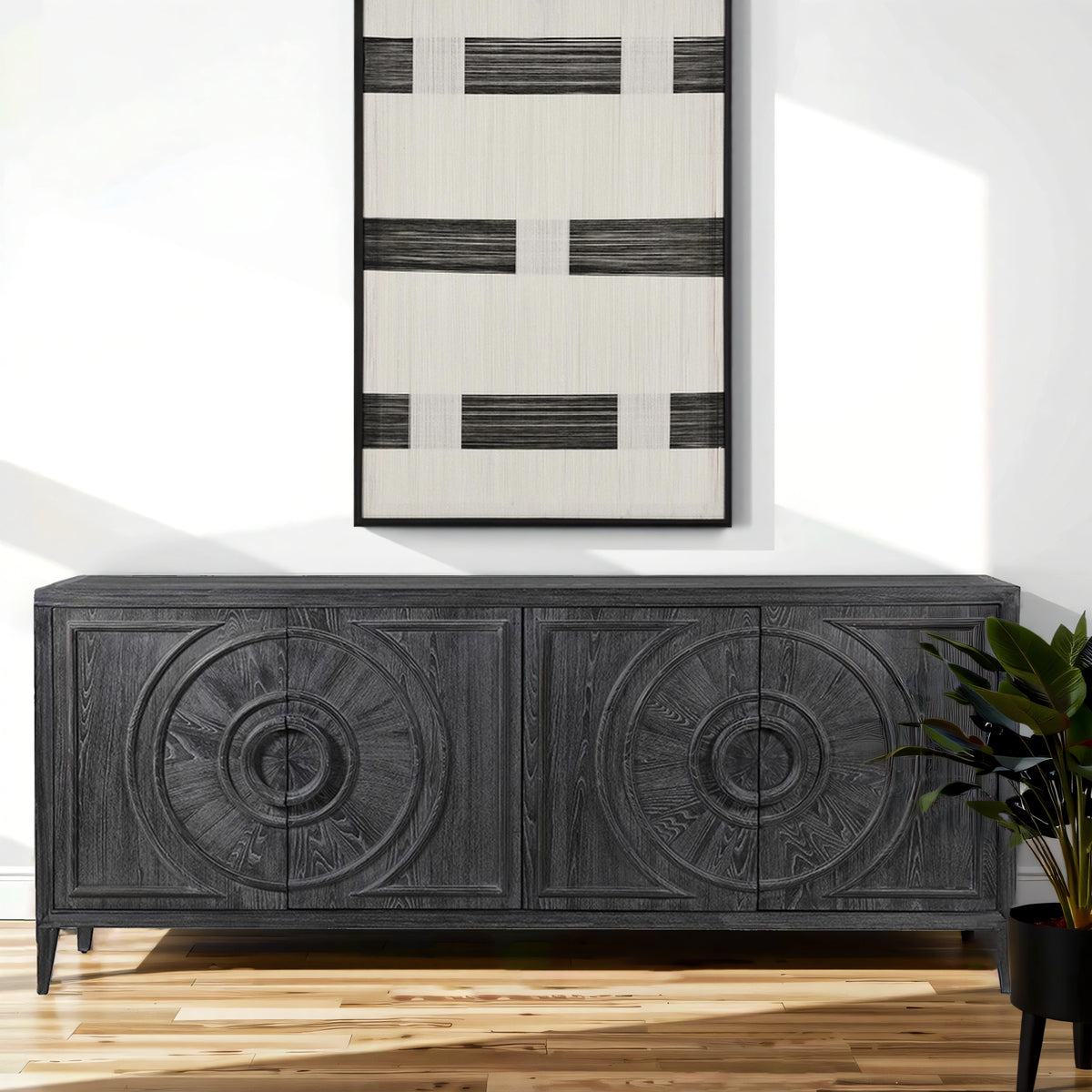 Dark wooden sideboard with decorative carvings in a room with a plant and abstract art on the wall.
