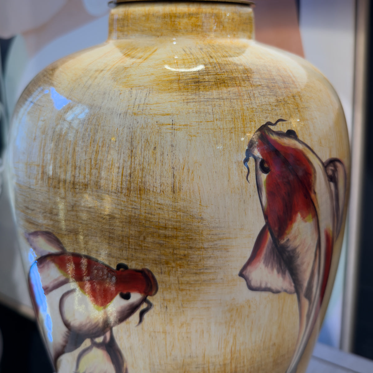A close-up of a glossy ceramic lamp with a textured beige and gold glaze, decorated with hand-painted koi fish in red, white, and black.