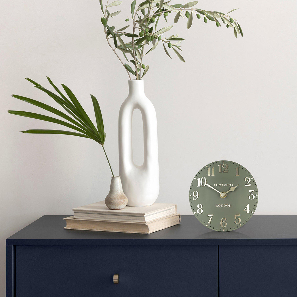 Decorative clock on a dark surface with a vase and plants in the background