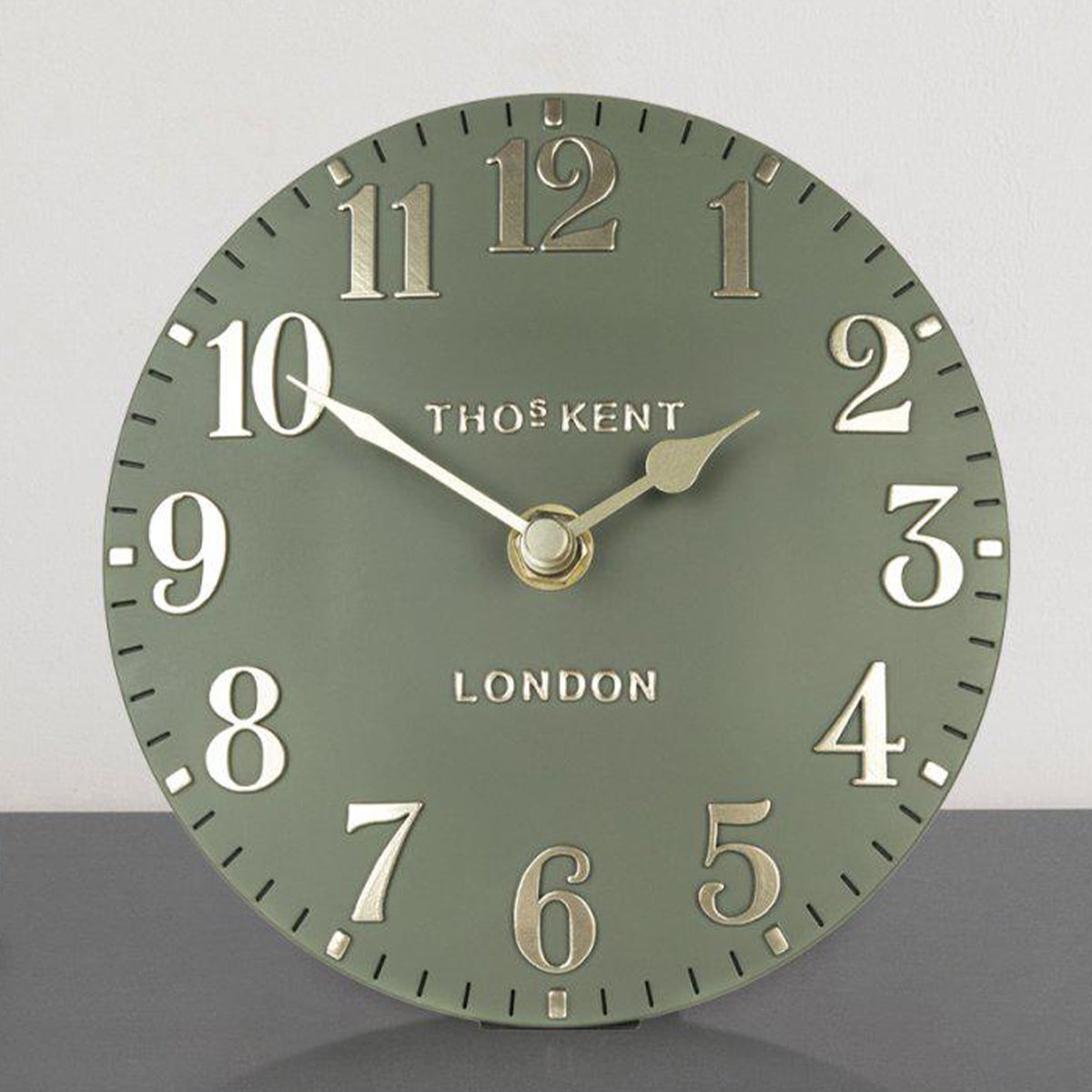 Green wall clock with gold numbers and brand name on a gray background