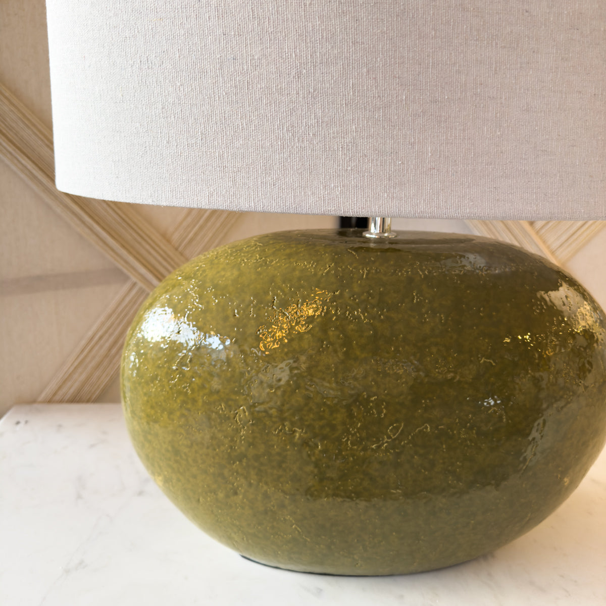 An olive green table lamp in an oval shape, with a white textured lamp shade.