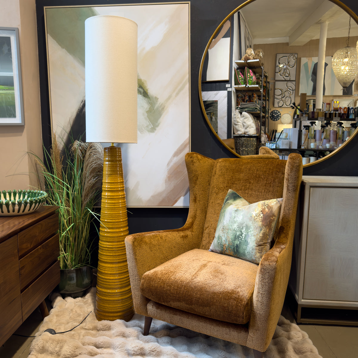 Cozy mid-century modern living room with rust orange armchair, sculptural mustard floor lamp, round mirror, abstract art, plants, and plush rug.