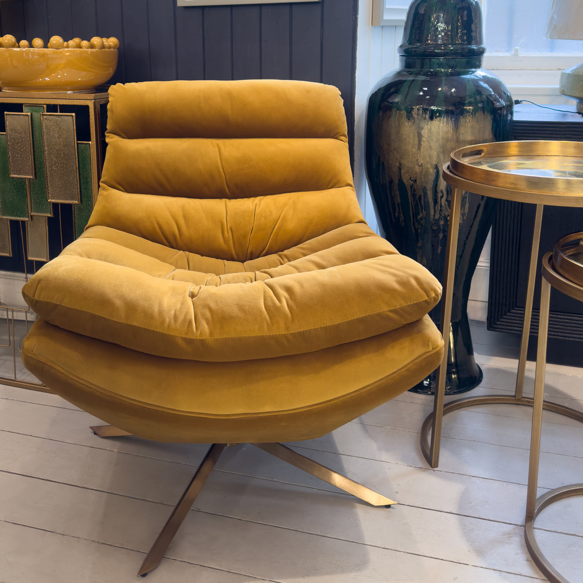 A yellow padded swivel chair next to gold nesting tables and a mustard bobble bowl.