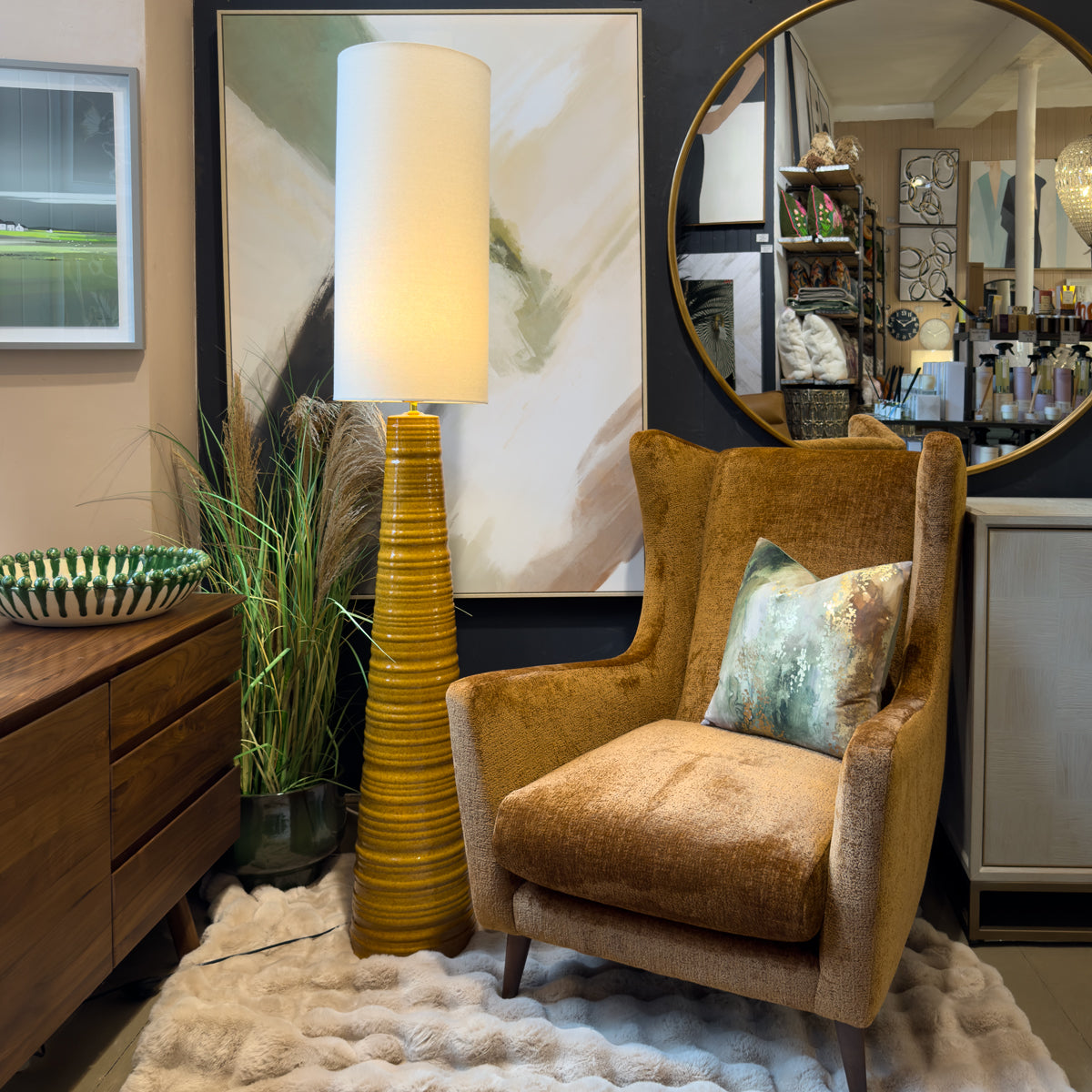 Cozy mid-century modern living room with rust orange armchair, sculptural mustard floor lamp, round mirror, abstract art, plants, and plush rug.