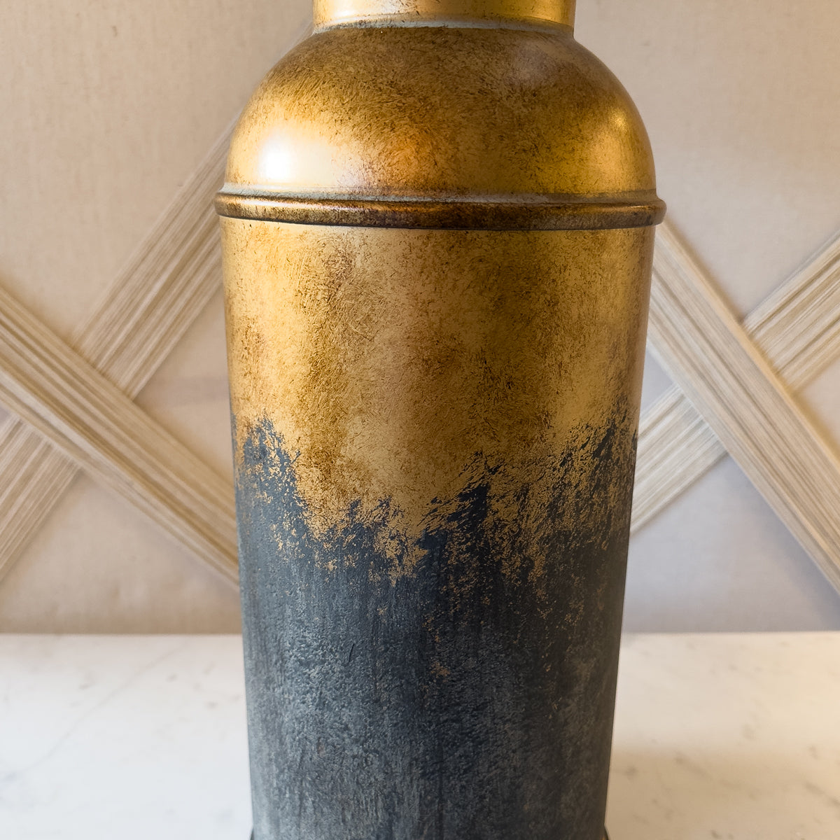 A close up of a bronze table lamp with a distressed, bottle shaped base.
