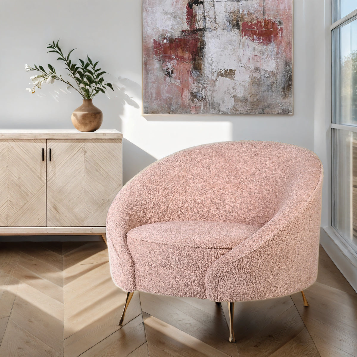 A pink curved tub chair infront of a washed wood sideboard and red & pink abstract artwork.