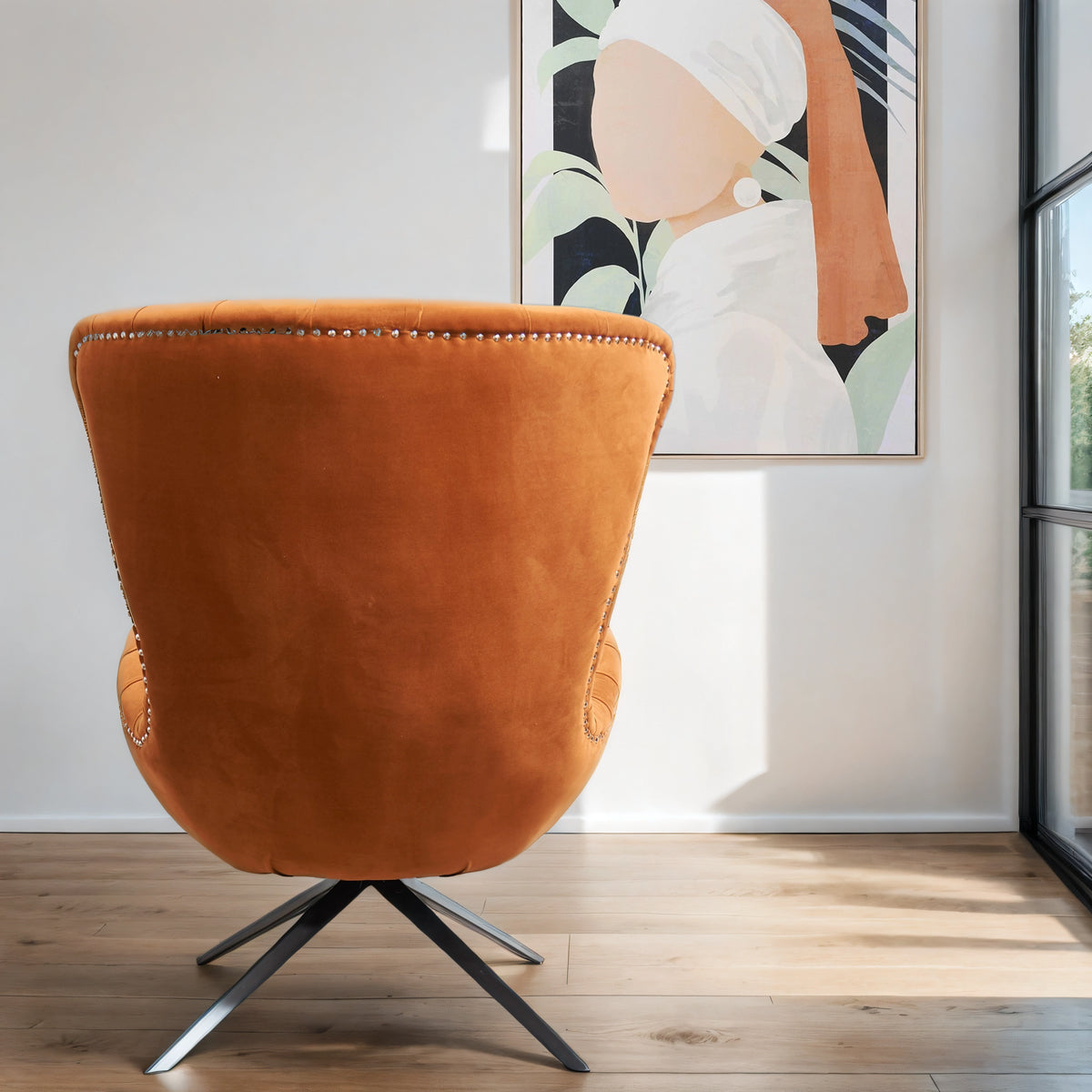 A back view of a rust accent chair with black legs, infront of a silhouette canvas in shades of black & orange.