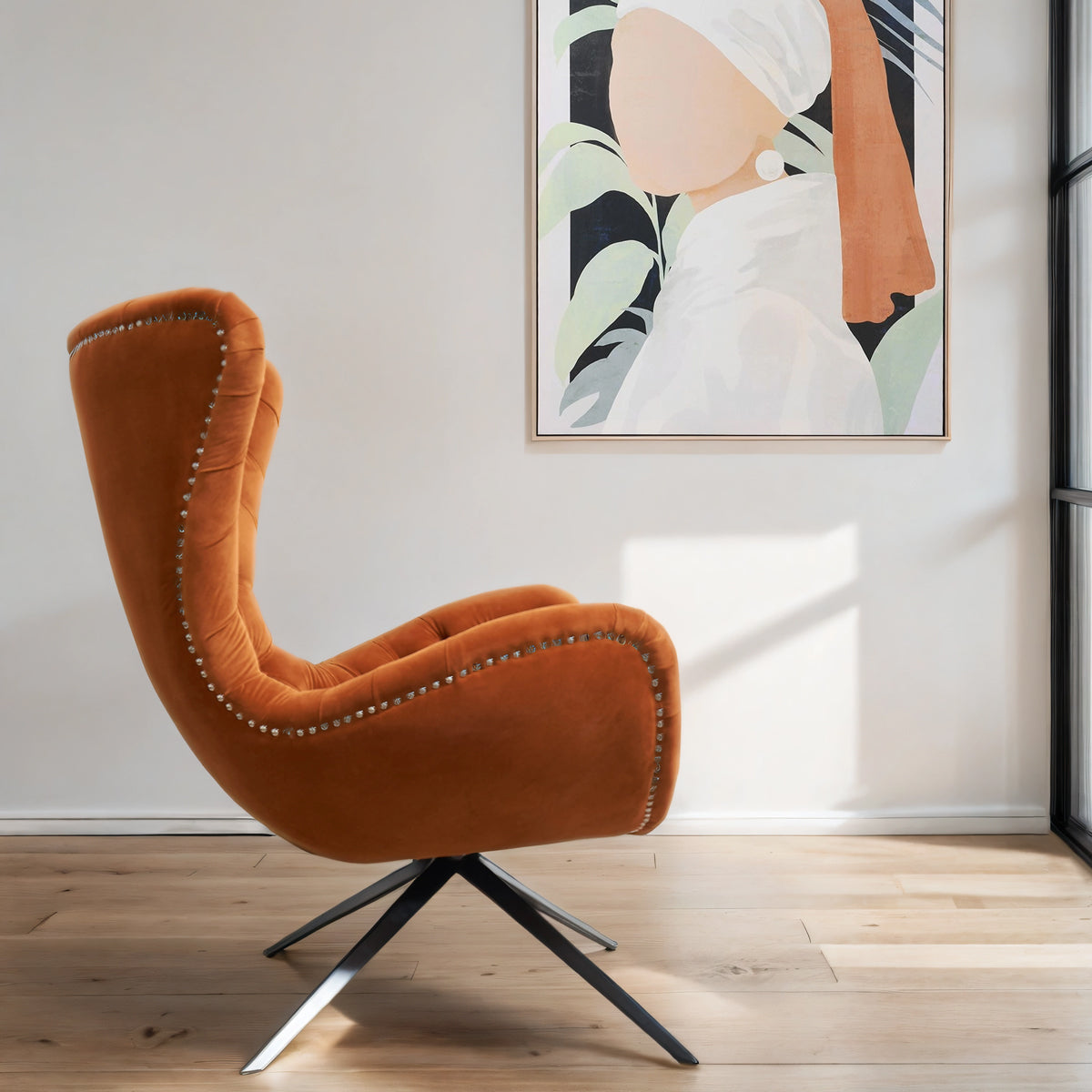 A side view of an orange buttoned occasional chair infront of an abstract canvas of a lady's head with foliage.